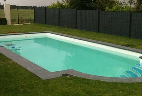 Rechteckiges Schwimmbecken mit gerundetem Treppenbereich und einem Beckenrand aus dunklen Steinplatten